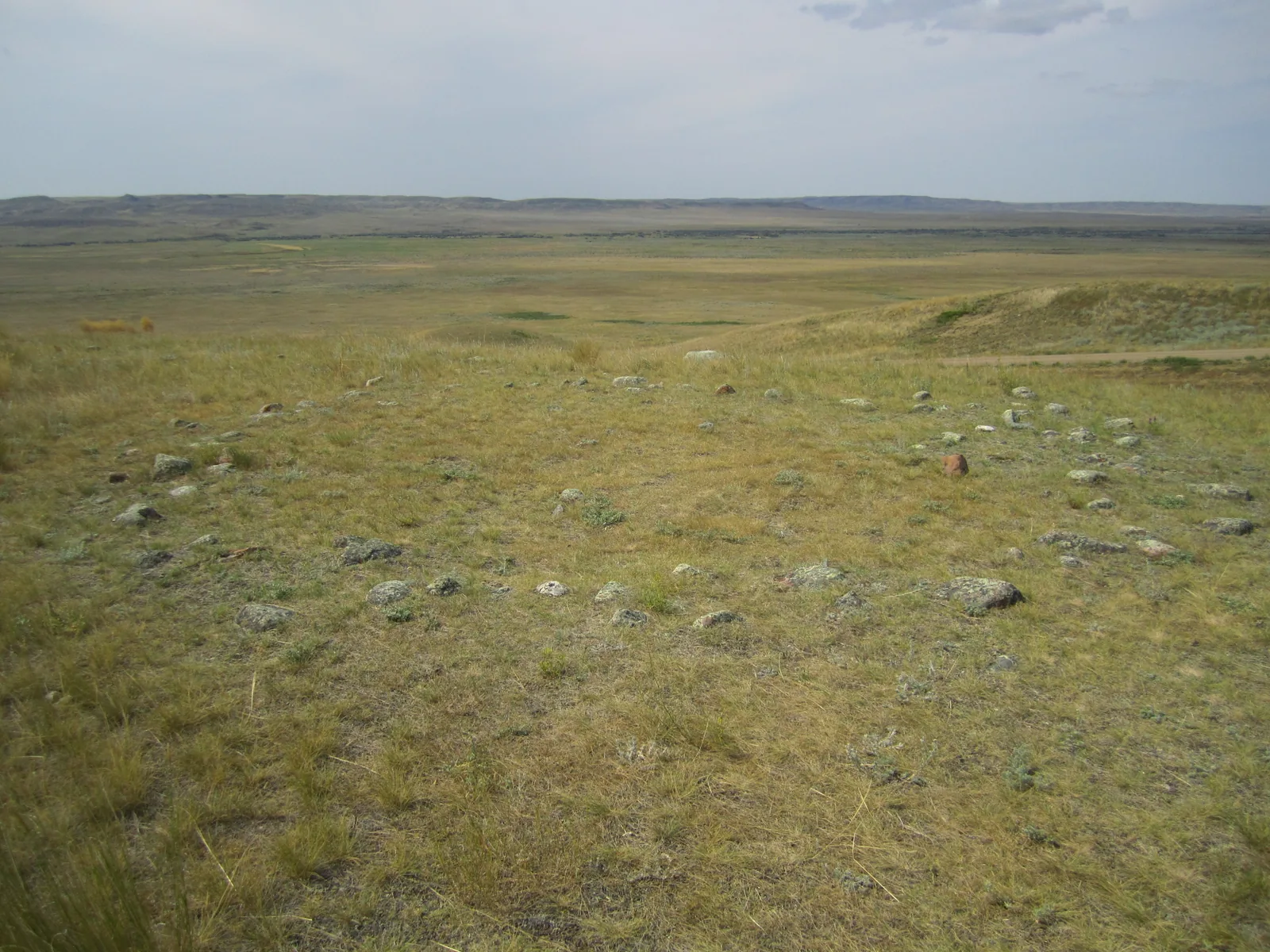 A circle of flat stones, a tipi ring, lies in the dry prairie grass of Grasslands National Park, a wide valley opening behind