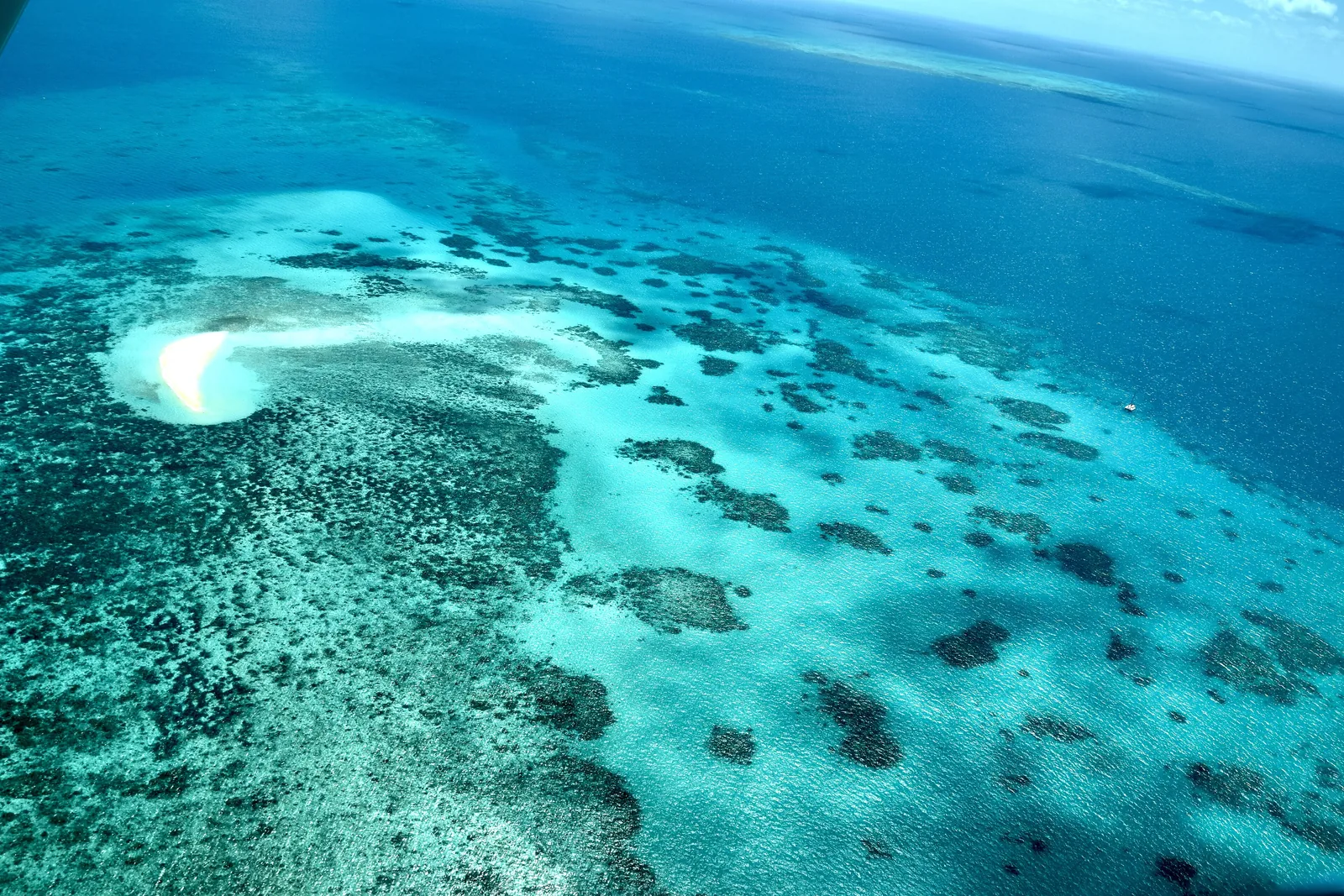 Aerial view of the Great Barrier Reef Marine Park: turquoise reef flats with dark coral heads and a pale sand bank in deep blue sea