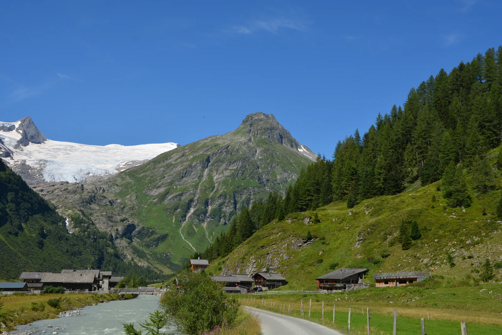 Alpine huts of Innergschlöss by the stream in Hohe Tauern National Park, a glacier below rocky peaks behind