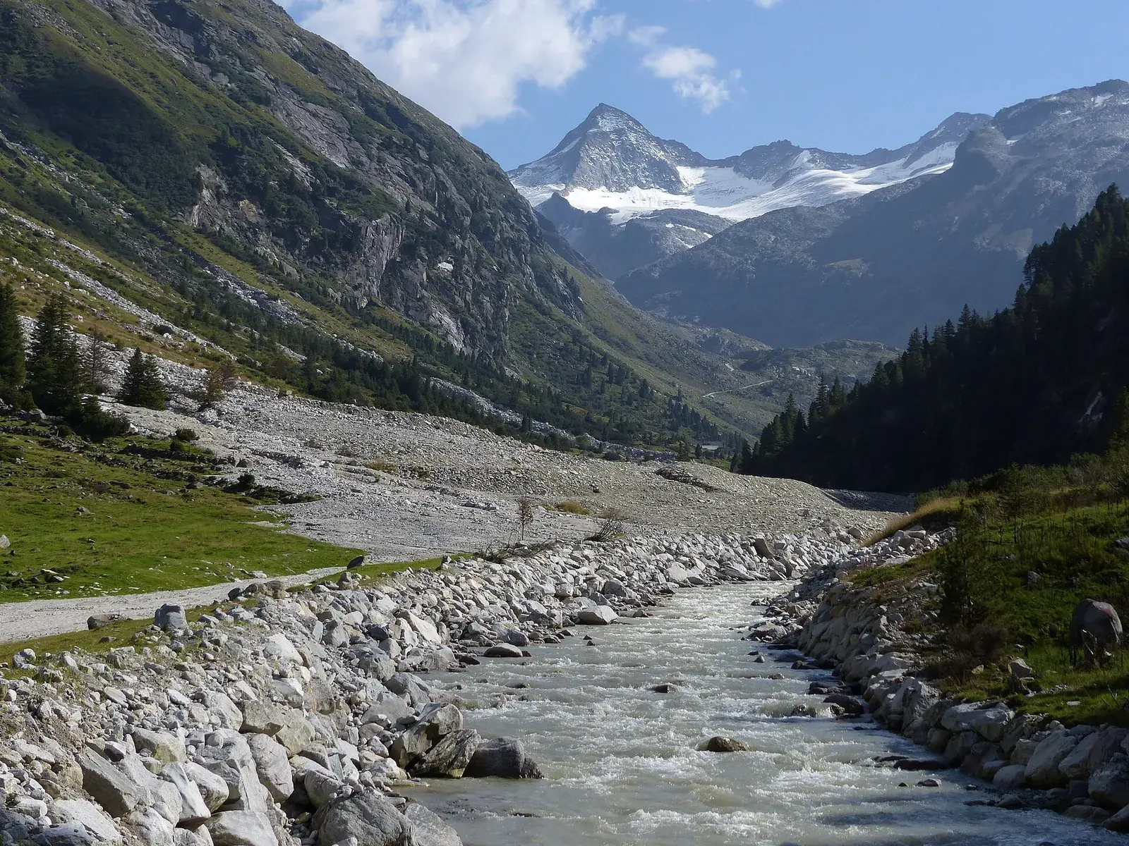 A glacier stream in Hohe Tauern National Park flows between pale stones through the Obersulzbach Valley, the glaciated summit of the Grosser Geiger behind