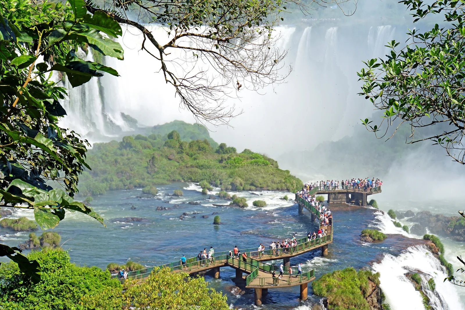 A walkway on the Brazilian side leads into the river in front of the Devil's Throat, visitors standing between waterfalls and spray