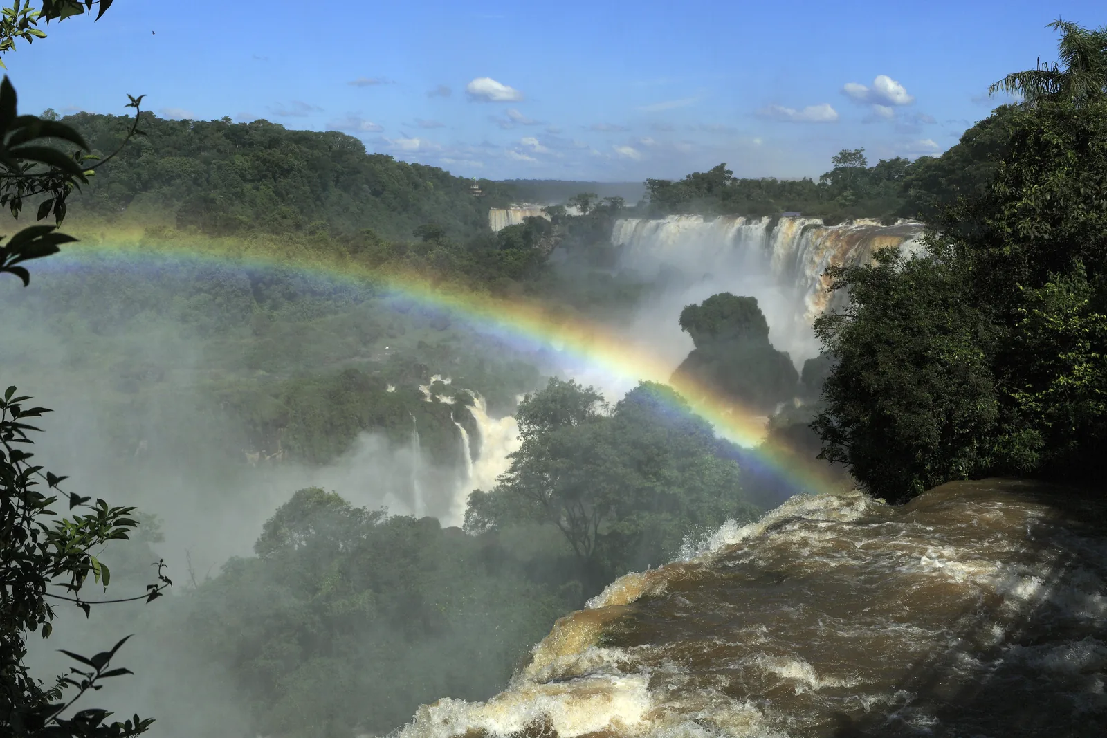 From the Upper Circuit at Iguazu Falls a rainbow arches over the gorge, with falls pouring out of the dense forest behind it