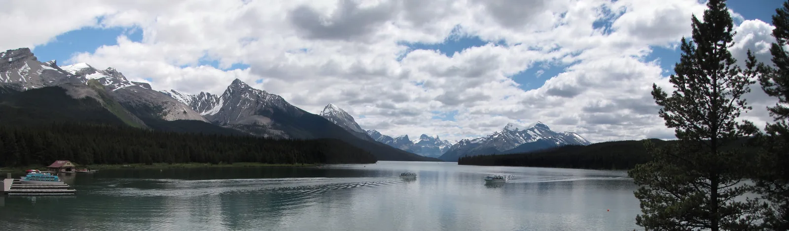 Panorama of Maligne Lake in Jasper National Park with the boathouse on the shore and a mountain range under clouds
