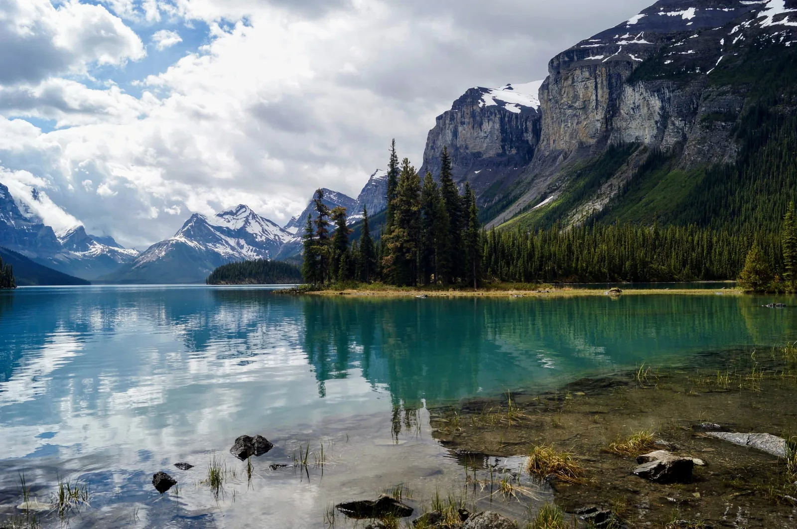 Spirit Island reflected in the calm water of Maligne Lake in Jasper National Park below rock walls