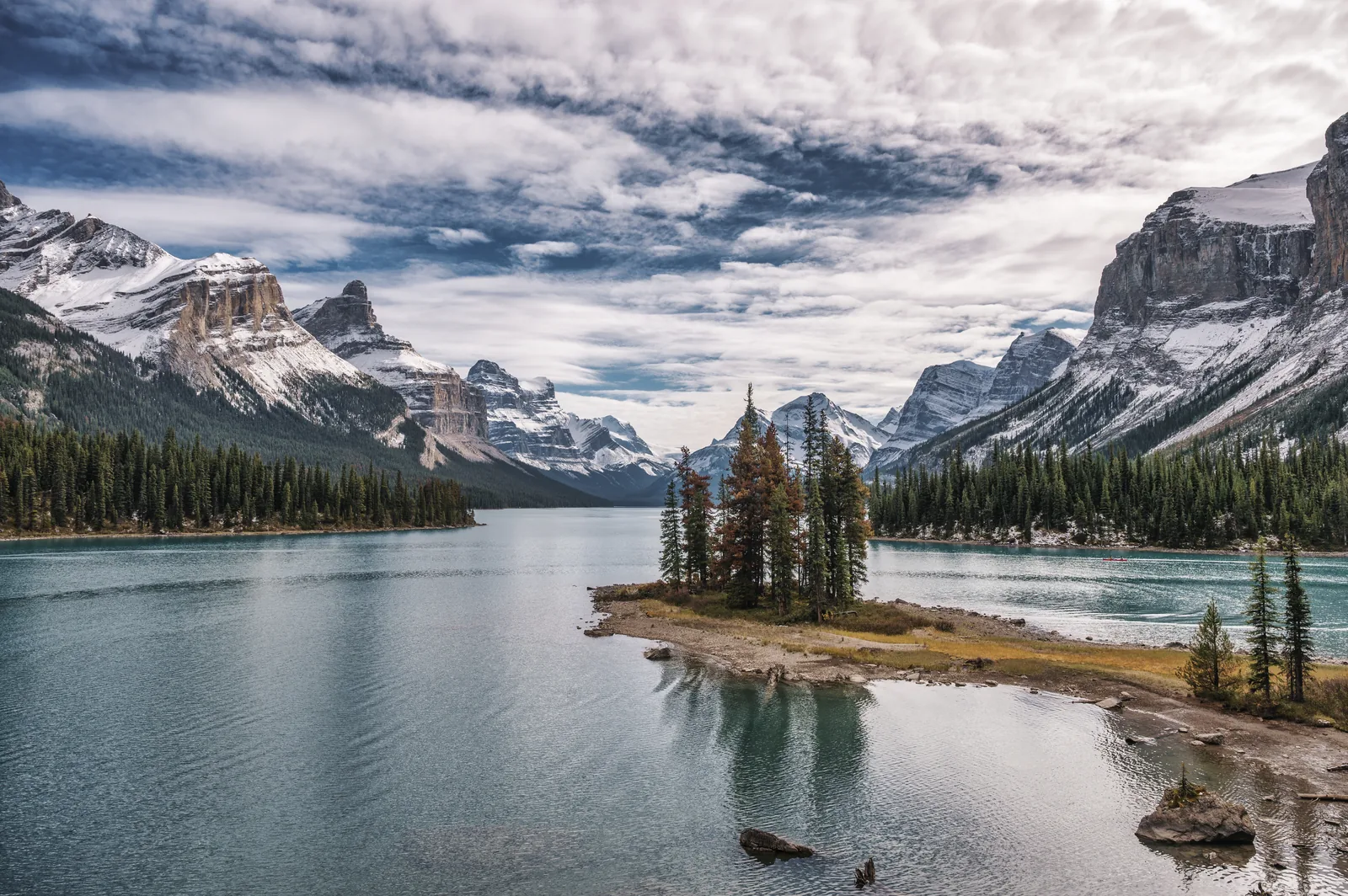 The forested spit of Spirit Island in Maligne Lake in Jasper National Park below snowy peaks