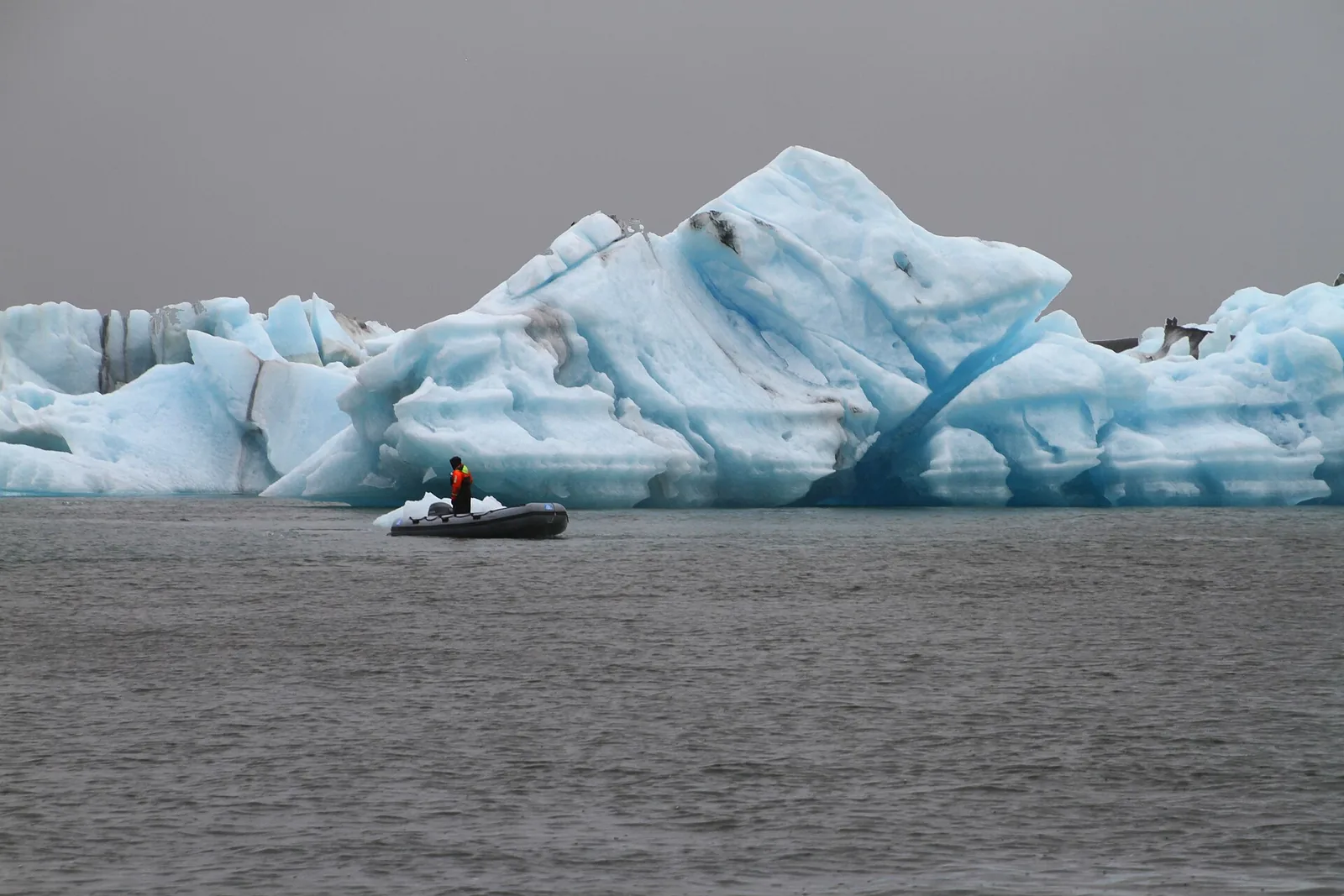 A Zodiac with a guide on Jökulsárlón in front of a large pale-blue iceberg