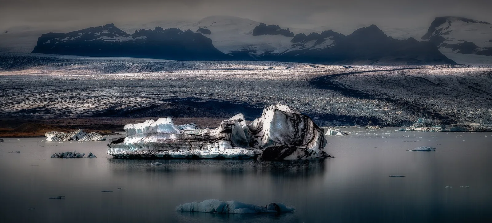 A dark-striped iceberg drifts on Jökulsárlón in front of the broad tongue of Breiðamerkurjökull
