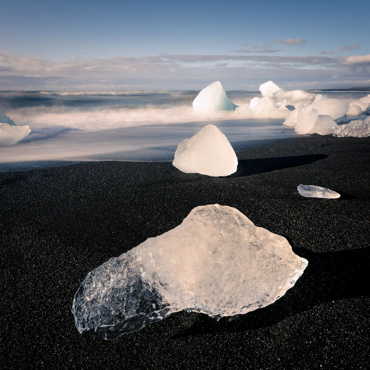 Clear chunks of ice from Jökulsárlón lie on the black sand of Fellsfjara against the light