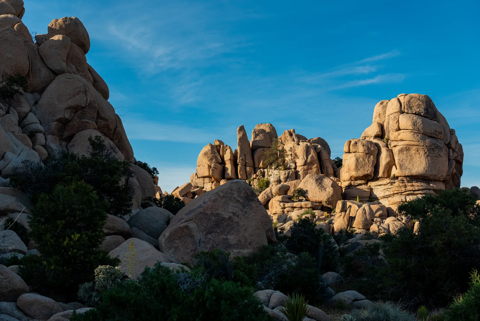 Stacked granite boulders in evening light above the scrub of Hidden Valley in Joshua Tree National Park