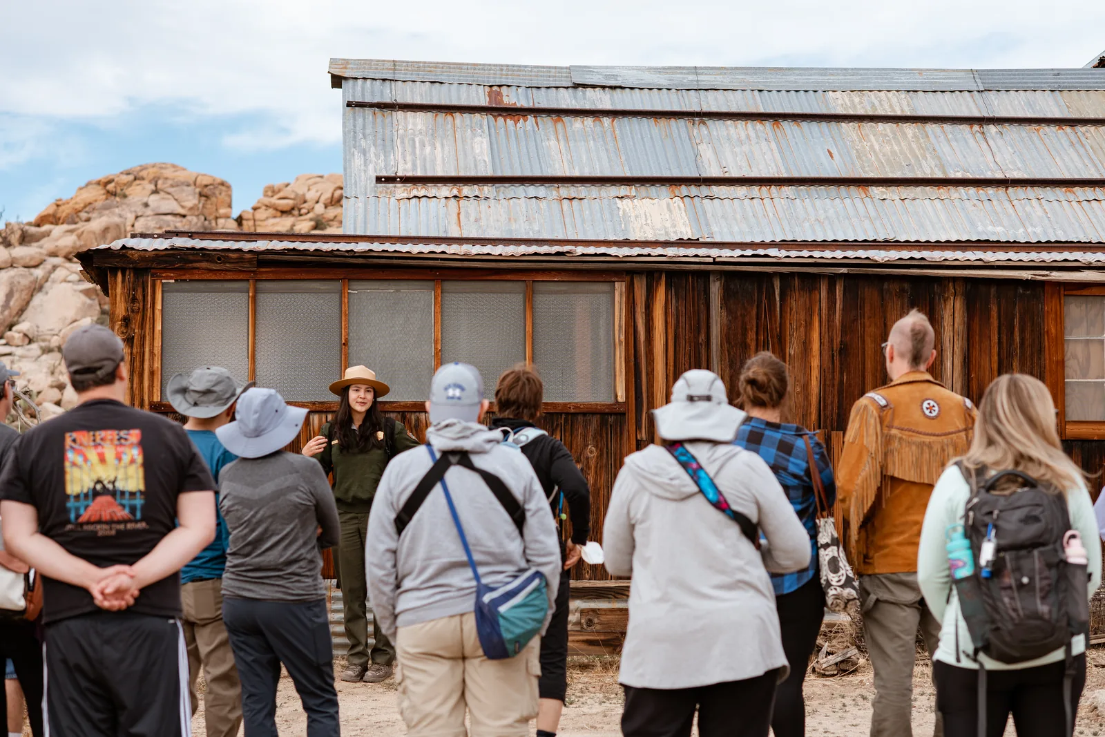 A ranger leads a group of visitors in Joshua Tree National Park in front of the wooden main building of the historic Keys Ranch