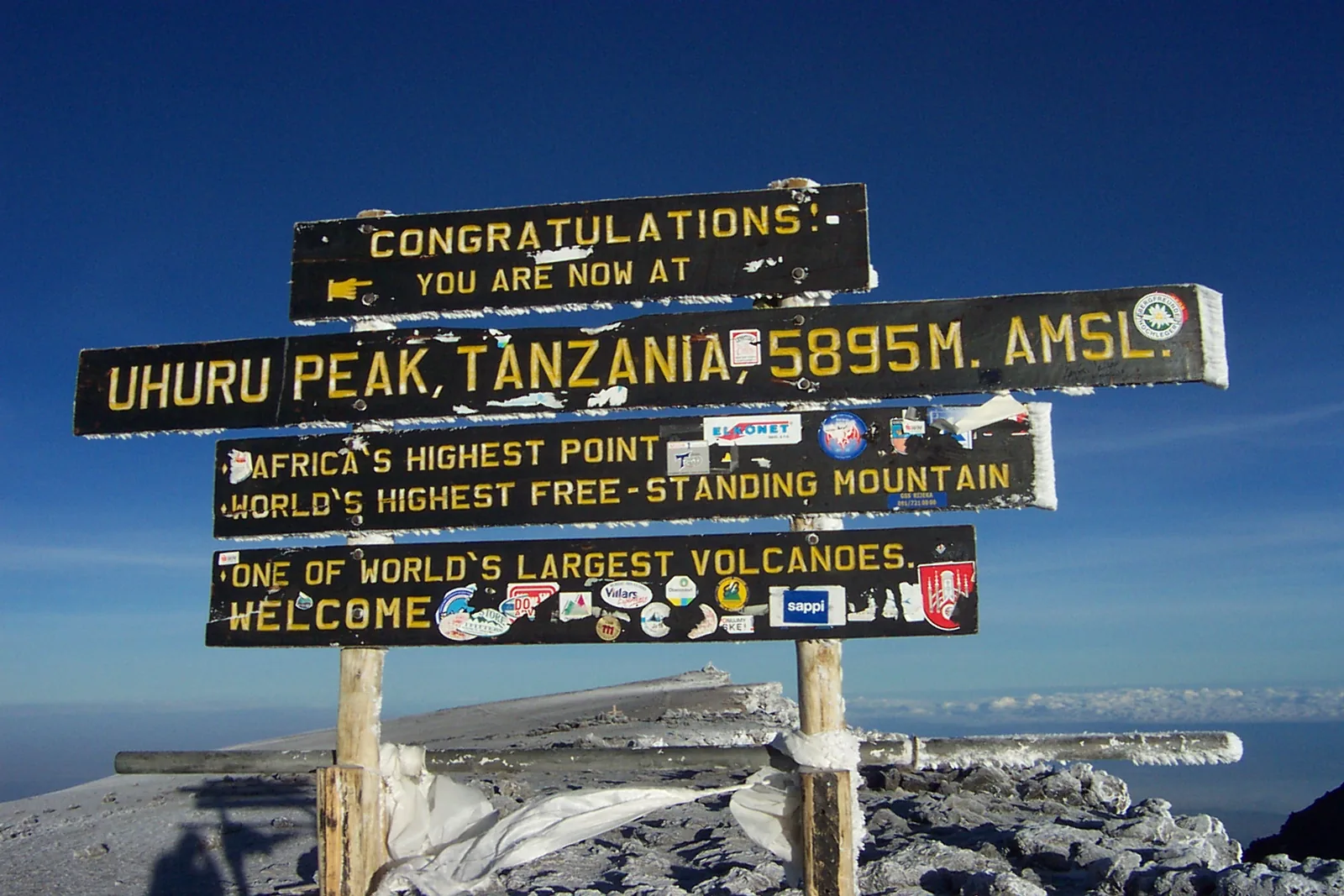 The wooden signs on Uhuru Peak in Kilimanjaro National Park showing the height of 5895 m against a deep blue sky