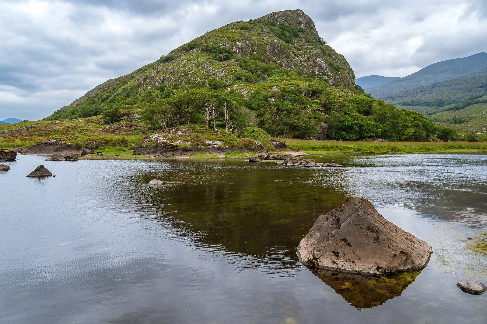 A lake in Killarney National Park between green hills and the Kerry mountains under a cloudy sky