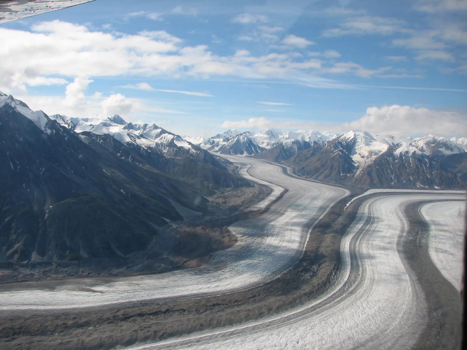 The Kaskawulsh Glacier in Kluane National Park with dark medial moraines through a wide valley, snow-covered peaks all around