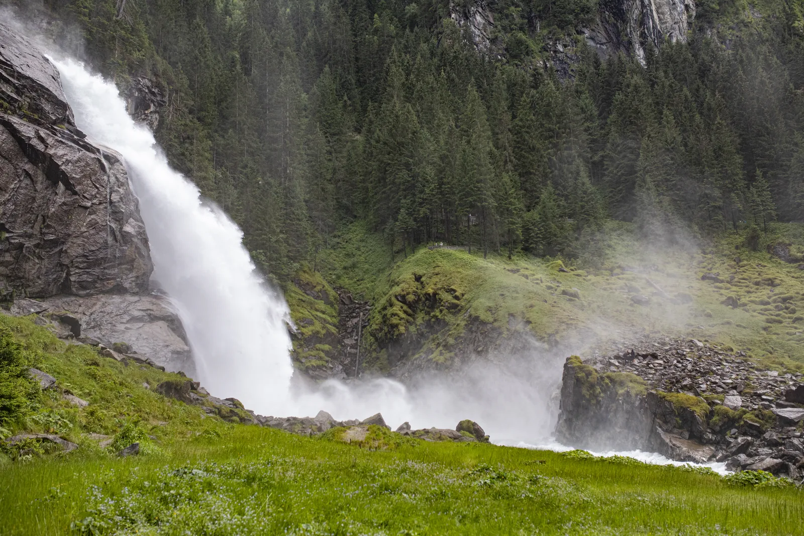The lower Krimml Waterfall plunges over a rock step, spray drifting across the meadow at the foot of the falls in Hohe Tauern National Park