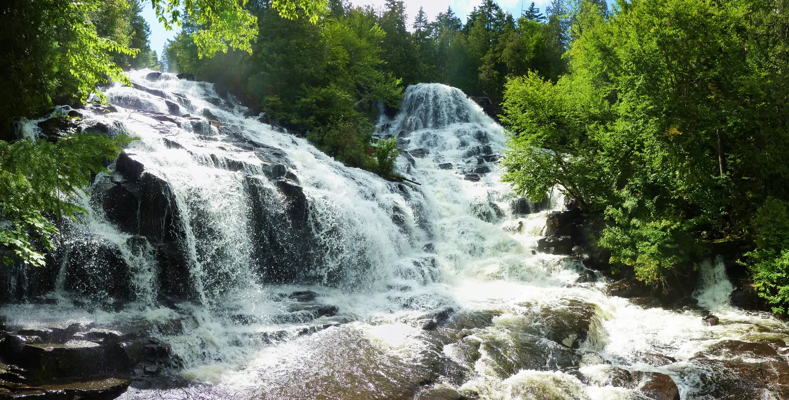 The Chutes Waber in La Mauricie National Park: a wide waterfall tumbles over several steps of dark rock, dense green broadleaf forest all around