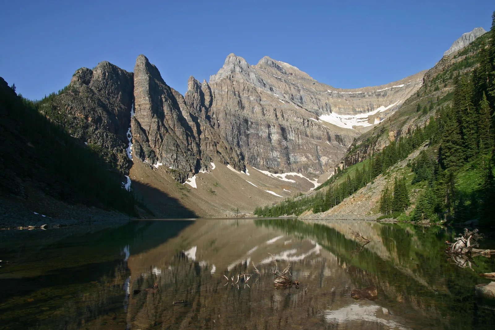 Lake Agnes in Banff National Park reflecting the rock walls of Mount Whyte, wooded slopes and snowfields in the cirque on the right.