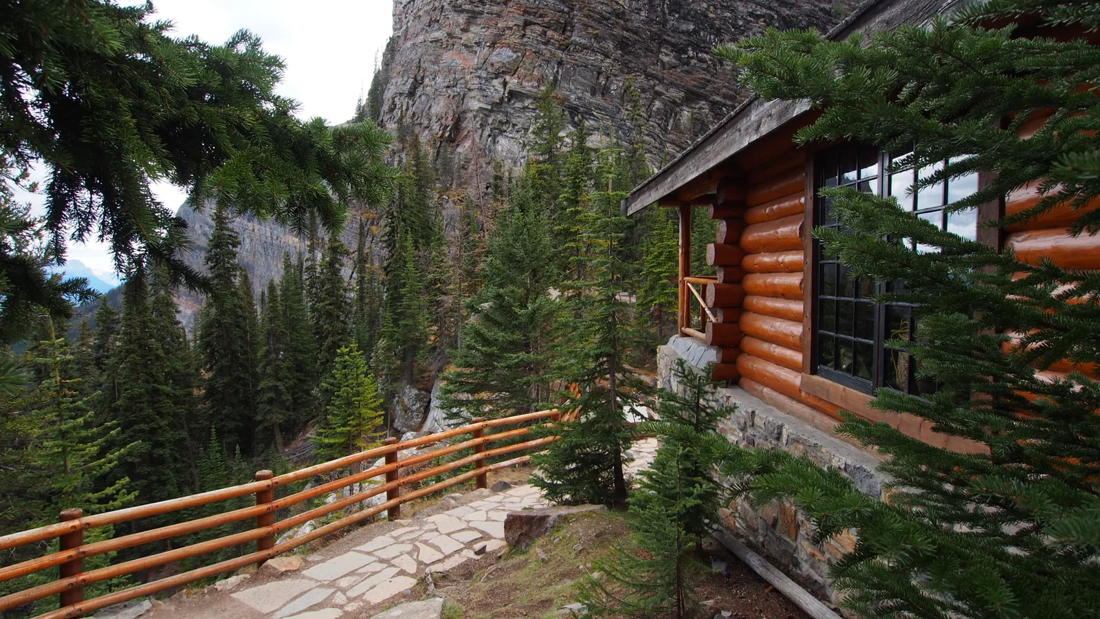 Lake Agnes Tea House in Banff National Park: a log building with a wooden railing and stone terrace among conifers below a rock face.