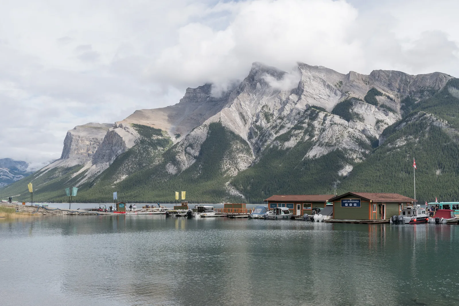 Boat dock at Lake Minnewanka in Banff National Park with the boathouse and tour boats, Mount Inglismaldie in cloud behind.