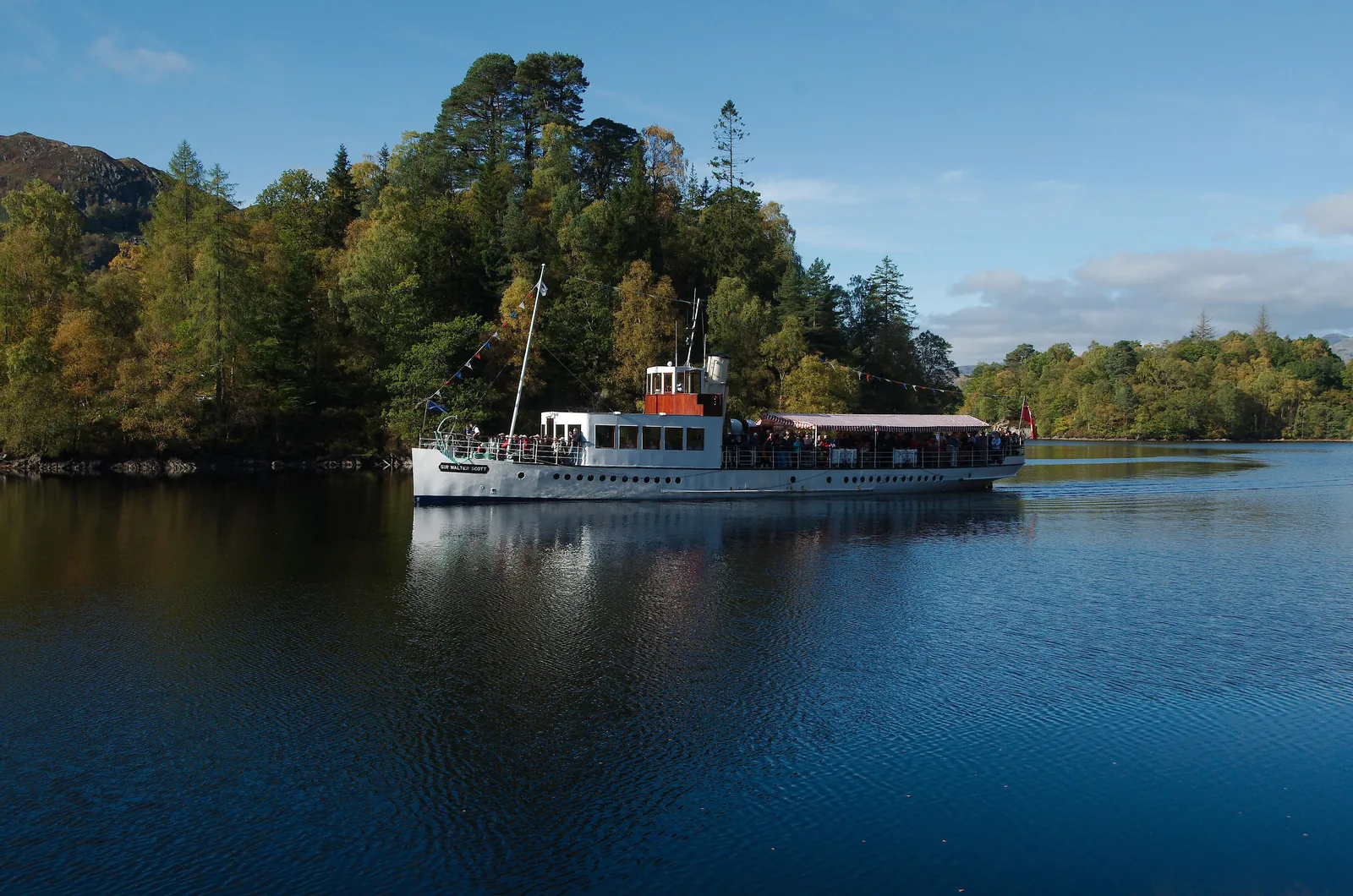 The steamship Sir Walter Scott on Loch Katrine in Loch Lomond & The Trossachs National Park in front of wooded shores