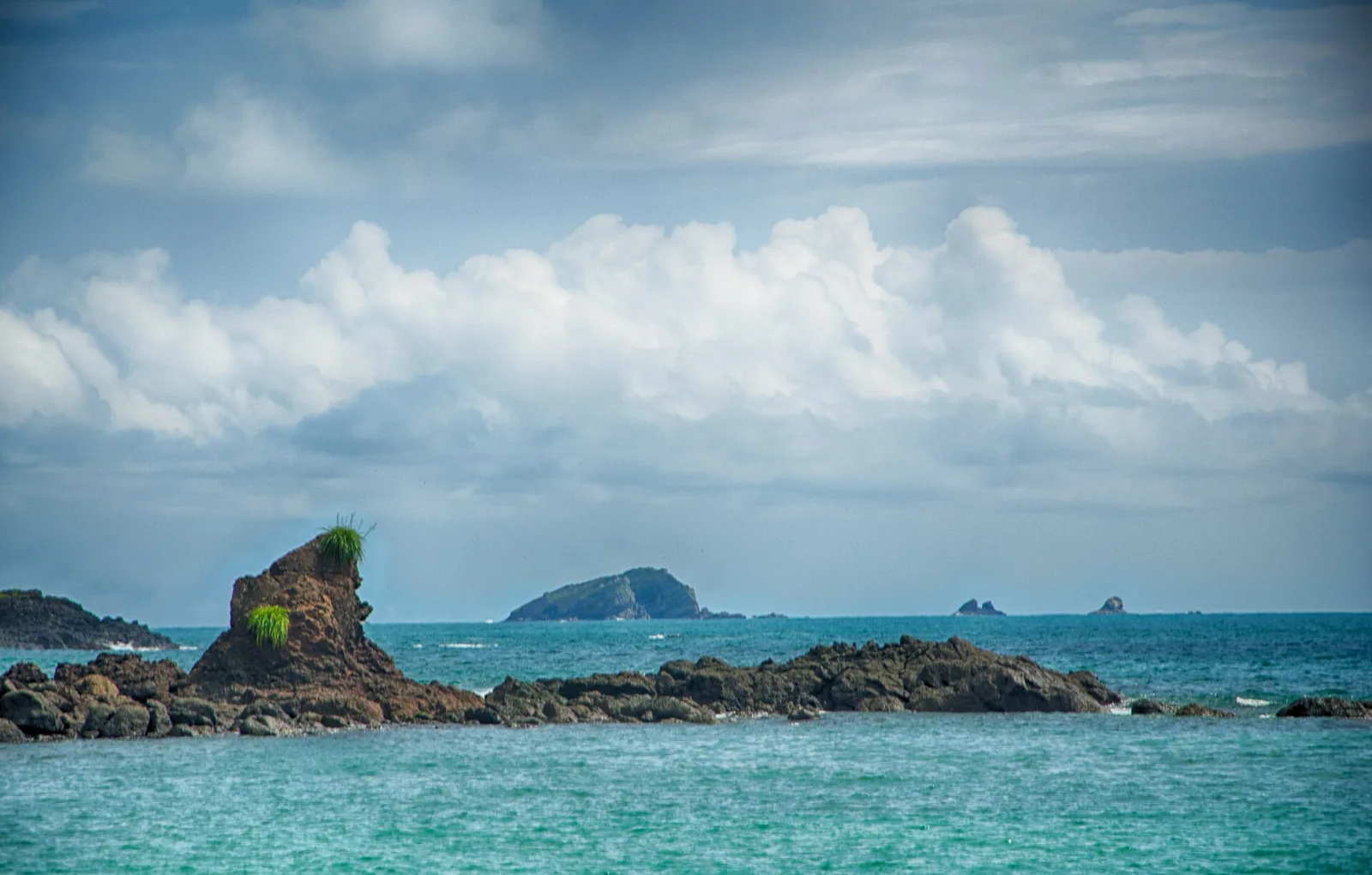 Sandy beach in Manuel Antonio National Park with dark rocks, waves and a forested coast