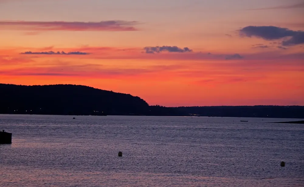 Sunset over the water off Bar Harbor, dark wooded island silhouettes under an orange-red evening sky