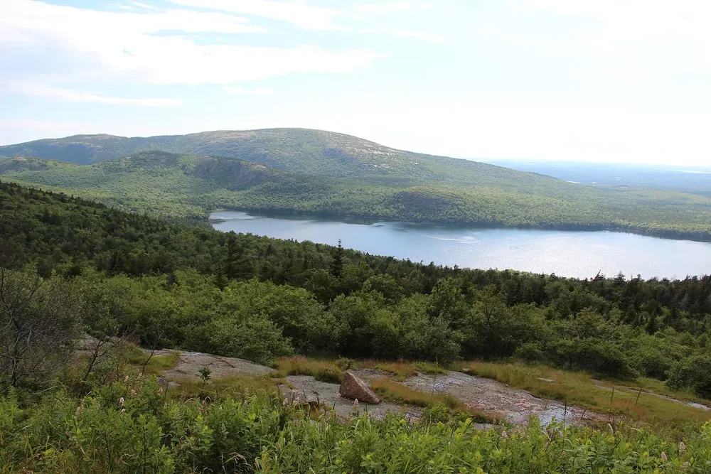 View over a granite slope and forest in Acadia National Park down to the long Eagle Lake, with a wooded ridge behind
