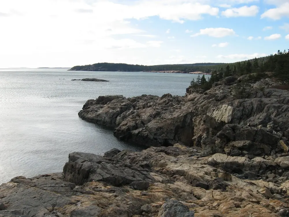 Rocky granite coast at Great Head in Acadia National Park, looking west across the sea to wooded headlands