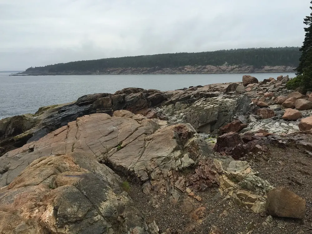 Granite slabs and boulders at Otter Point in Acadia National Park, looking west across the sea to a wooded coast