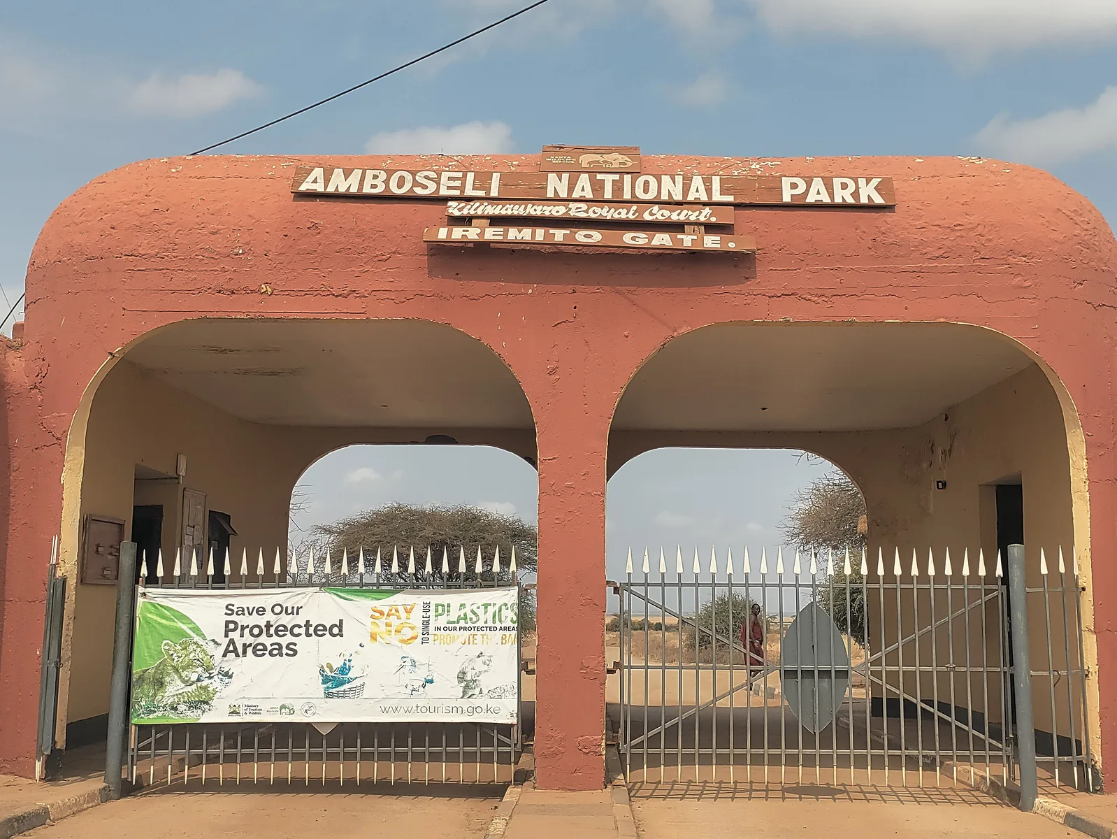 Iremito Gate of Amboseli National Park: a red-brown gate building with two arches and the sign Amboseli National Park, a closed metal gate in front