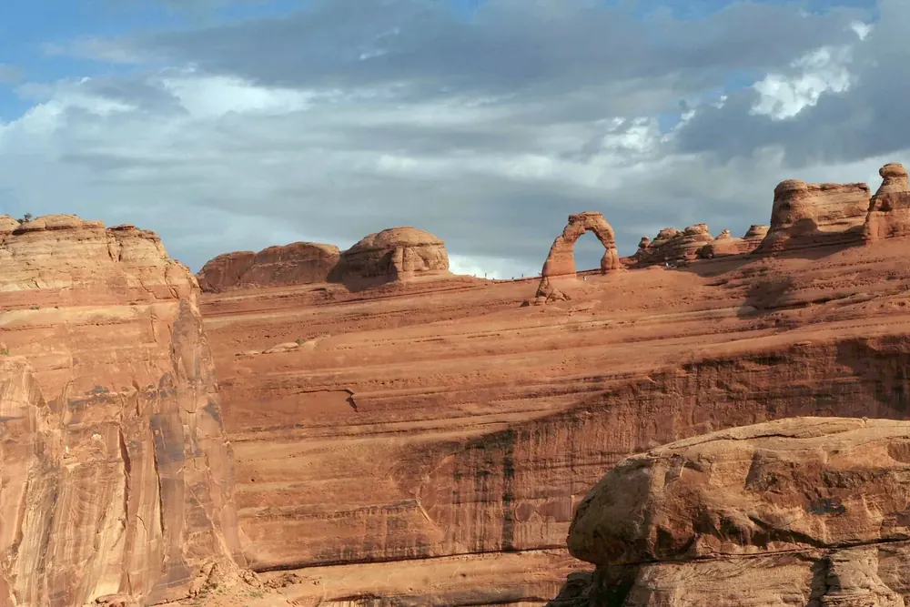View from Delicate Arch Viewpoint in Arches National Park across a gorge to Delicate Arch on its red sandstone ridge