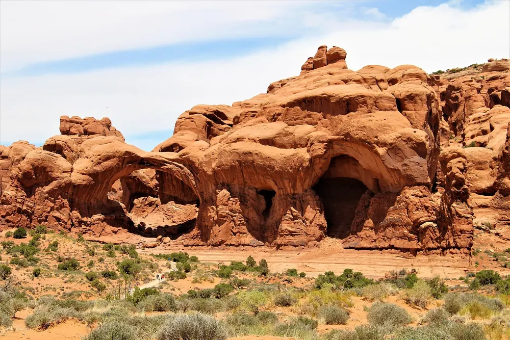 Double Arch in Arches National Park: two interlocking sandstone arches in a red rock wall, low desert vegetation in front