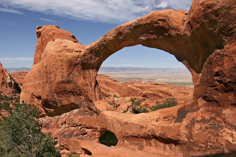 Double O Arch in Arches National Park: a large oval sandstone arch above a smaller hole in the rock, with a view through to the wide plain