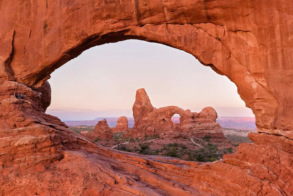View through the glowing red rock arch of North Window in Arches National Park to Turret Arch and the plain beyond