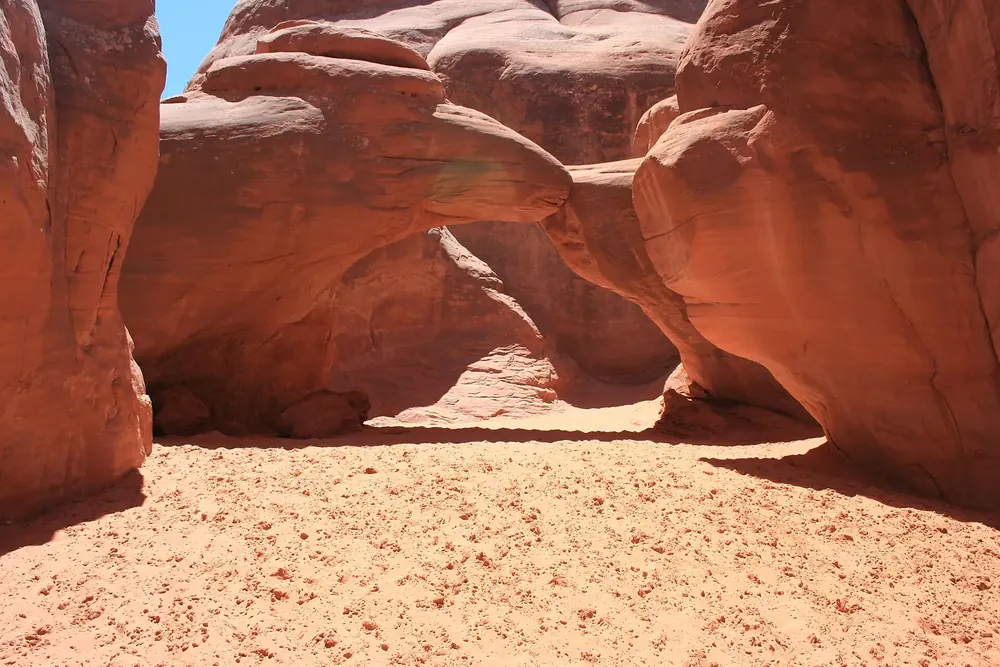 Sand Dune Arch in Arches National Park: a low sandstone arch between narrow red rock walls, fine reddish sand beneath