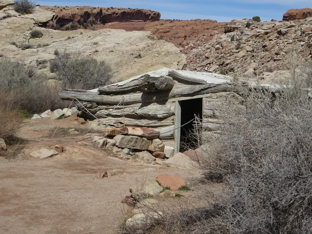 Historic root cellar at Wolfe Ranch in Arches National Park, made of weathered timber beams, set into a slope among desert shrubs