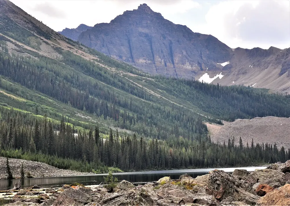 Consolation Lakes in Banff National Park: scree shore on the mountain lake, forested slopes and the rock face of Mount Bell behind.