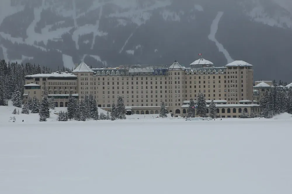 Fairmont Château Lake Louise in Banff National Park in winter, with the frozen, snow-covered lake and snowy conifer forest in front.