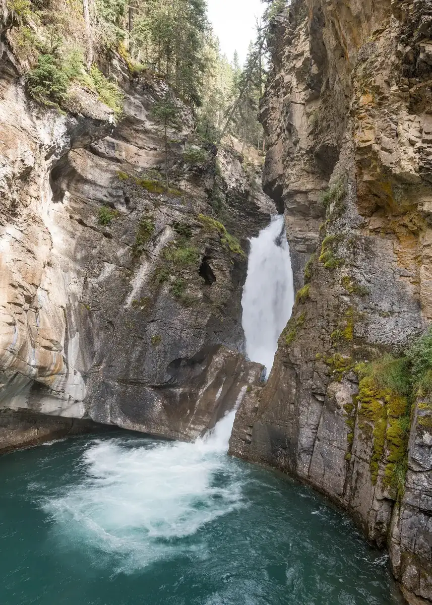 Lower Falls in Johnston Canyon in Banff National Park: a waterfall plunges through a narrow limestone gorge into a turquoise pool.