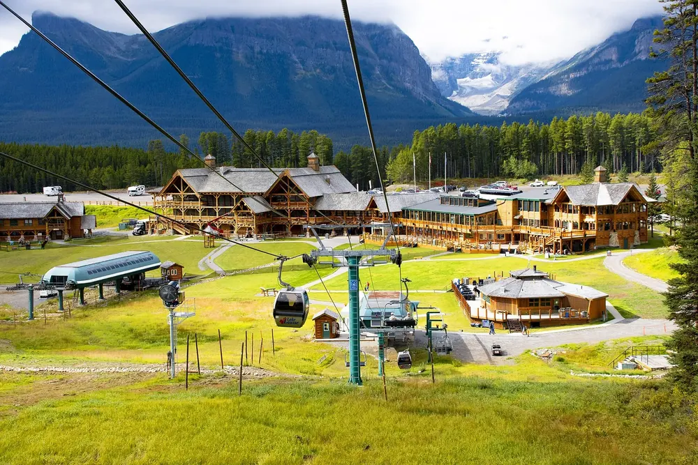 Base area of the Lake Louise ski resort in Banff National Park in summer: gondola, wooden lodges and green meadows below forested mountains.