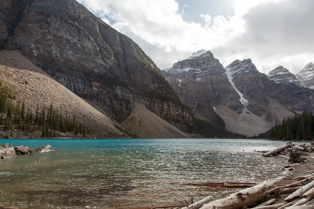 Moraine Lake in Banff National Park near the shuttle stop: turquoise water with driftwood below scree slopes and rugged peaks.