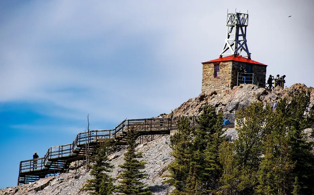 Historic stone weather station on Sanson Peak in Banff National Park, wooden stairs and boardwalks on the rocky summit in front.