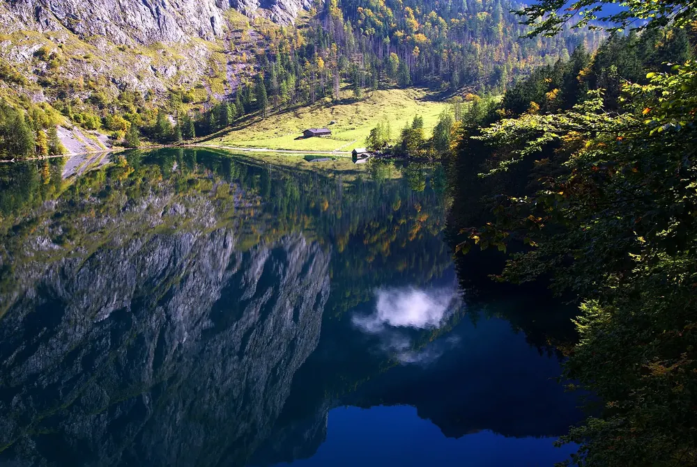 The Obersee in Berchtesgaden National Park, reflecting the rock walls, at the end of the lake the meadow of the Fischunkelalm with its huts