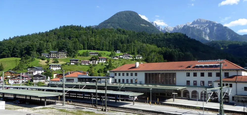 Berchtesgaden Hauptbahnhof (main station) from the north-west: platforms and station building, wooded slopes and peaks behind