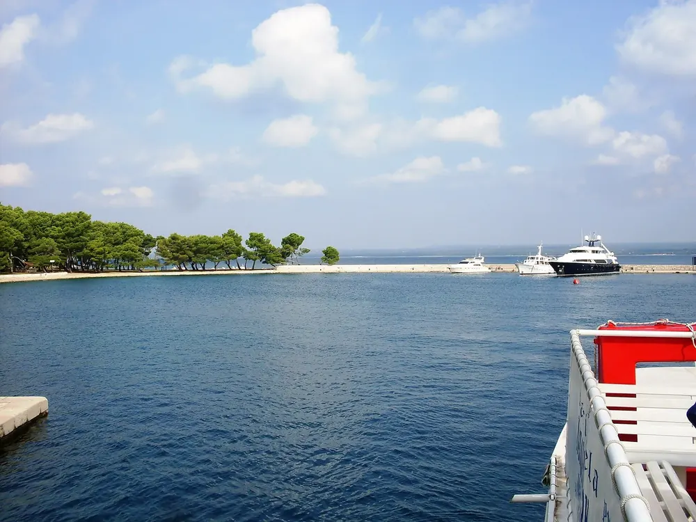 Veliki Brijun harbour in Brijuni National Park: a calm blue harbour basin with a jetty, pines on the shore and boats at anchor