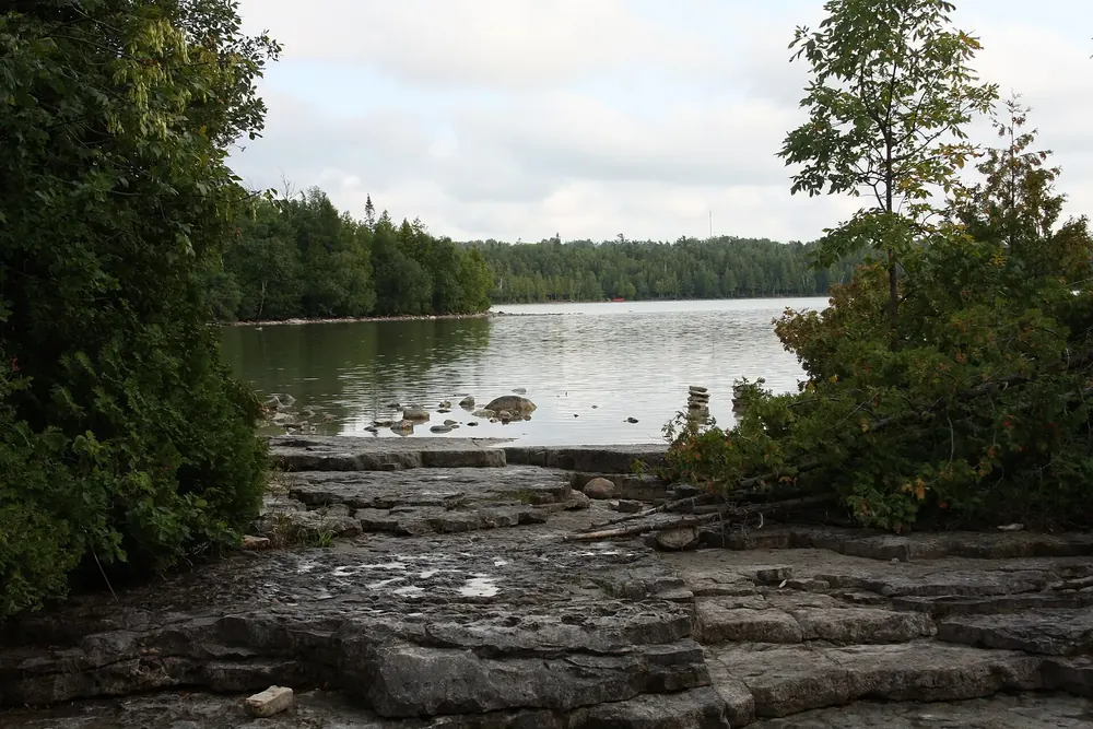 Cyprus Lake in Bruce Peninsula National Park: flat limestone slabs on the shore, calm water and dense conifer forest on the far bank