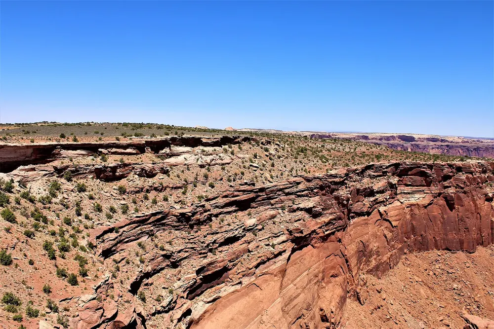 View from Buck Canyon Overlook in Canyonlands National Park across red sandstone steps and canyon rims to the wide horizon