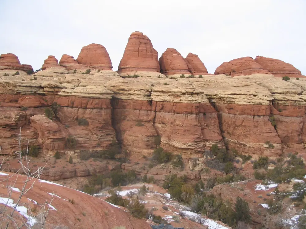 View near Elephant Hill in Canyonlands National Park: red rock ledges and rounded sandstone towers of the Needles with patches of snow