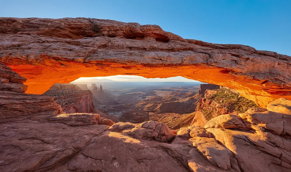 Mesa Arch in Canyonlands National Park at sunrise: the underside of the rock arch glows orange, with the view into the canyon country below