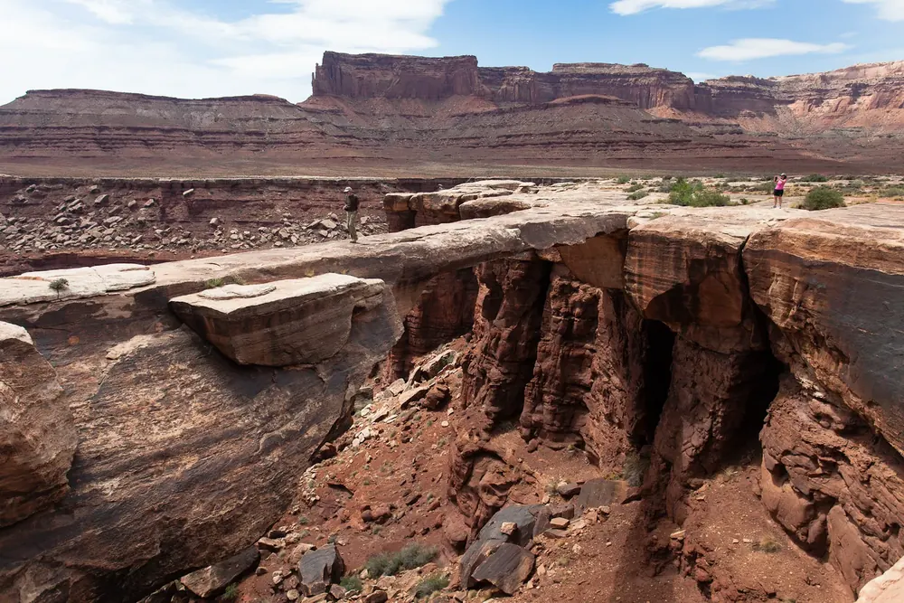 Musselman Arch in Canyonlands National Park: a flat sandstone arch over a deep rock crevice, red mesas on the horizon behind