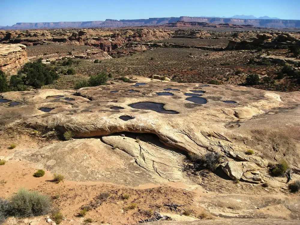 Pothole Point in Canyonlands National Park: rainwater-filled hollows in pale sandstone, with wide canyon country and mesas behind